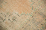 Vintage distressed Oushak rug texture showing even wear, visible foundation, and muted apricot and green motifs.