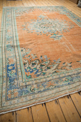 Distressed corner of a vintage Oushak rug, faded apricot and blue blossomed florals, visible wear.