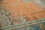 Distressed Oushak carpet's apricot orange field with faded mint green floral elements and aged texture.