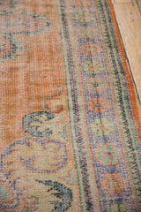 Distressed vintage Oushak rug's worn apricot orange pile, visible foundation, and pale blue vinery.