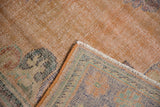 Distressed Oushak rug corner showing worn apricot pile and visible woven foundation.