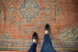 Distressed Oushak rug, brick red and blue motifs, with visible even wear underfoot.