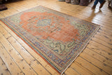 Distressed Oushak carpet corner, with worn brick red pile and floral patterns in blue, green.