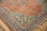 Distressed Oushak rug corner shows brick red field, pale blue and ivory floral border.
