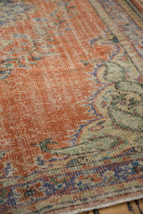 Distressed pile of a vintage Turkish Oushak rug with faded brick red, blue, and green floral vinery.