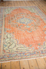 Vintage Oushak carpet corner with distressed pale brick red field, faded blue patterns, and ivory fringe.