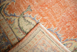 Distressed vintage Oushak carpet folded, revealing worn orange pile and pale foundation.