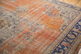 Distressed Oushak rug showing worn terra cotta field, Rococo vinery, and navy blue border.