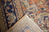 Distressed Oushak rug corner reveals faded brick red, navy, ivory pile and woven reverse.