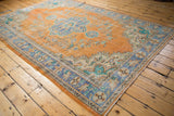 Distressed pile texture on vintage Oushak rug corner, showing faded orange and royal blue floral border.