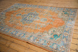 Distressed pile on a vintage Oushak rug revealing faded orange and intricate blue-turquoise border.
