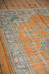 Faded distressed texture on the Oushak rug's tangerine orange field and royal blue border.