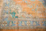 Distressed vintage Oushak rug with faded terra cotta, blue, turquoise border, showing foundation.