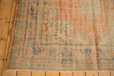 Distressed Oushak rug corner, showcasing muted apricot, mint, blue patterns and visible wear to foundation.