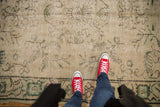Distressed Oushak carpet showcasing worn texture, pale green floral motifs.