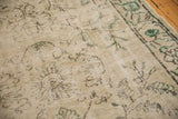 Close-up of distressed vintage Oushak rug, showing muted green Arts & Crafts floral motifs and border.