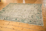 Distressed Oushak rug corner with pale sea foam and mint green scrolling floral motifs, charcoal border.