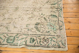Distressed Oushak carpet corner, displaying pale green scrolling tendrils and low pile.