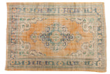 Distressed vintage Oushak carpet with an apricot field, ivory scalloped medallion, and dusty teal details.