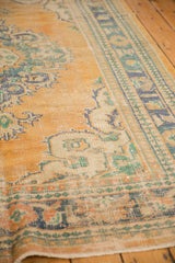 Distressed Oushak carpet showing pile wear, featuring faded apricot, teal, and ivory patterns.