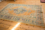 Distressed corner of a vintage Oushak carpet, showing pale apricot, dusty teal, and ivory tones with worn texture and foundation visible.