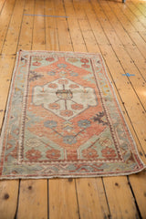 Distressed vintage Oushak rug runner corner showing brick red, sea foam green, beige pattern, and fringe.