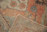 Folded corner of distressed Oushak rug: worn blush red pile, fringe, and hand-knotted foundation.