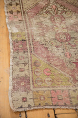 Distressed Oushak rug corner: faded aubergine, sage, worn pile, and visible foundation.