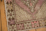 Corner of distressed Oushak rug showing geometric patterns, dusty pink, sage, and visible wear.