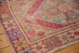 Distressed Oushak rug corner showing even wear on geometric blush and blue patterns.