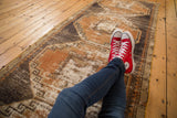 Distressed Oushak runner with rust and charcoal geometric medallions, casually styled with red sneakers.