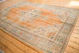 Vintage distressed Oushak carpet showcasing worn orange field and decorative celadon green border.