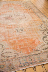 Distressed orange and ivory vintage Oushak rug showing muted border pattern and fringe.