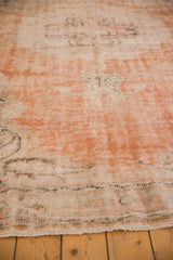 Decorative distressed texture of vintage Oushak rug, showing faded orange, ivory, and fringe.
