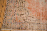 Distressed Oushak rug corner, showing faded orange and blue tones on the detailed border.