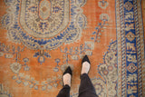 Distressed Oushak rug, burnt orange field with royal blue, ivory scrolling floral motifs, worn texture.