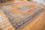 Distressed burnt orange Oushak rug, scrolling floral motifs, and royal blue curvilinear border.
