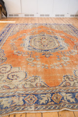 Distressed Turkish Oushak rug: faded burnt orange field, royal blue scrolling floral motifs.