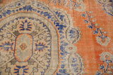 Distressed vintage Oushak rug showing worn burnt orange field and blue floral motifs.