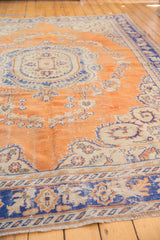 Distressed Oushak rug with burnt orange field, blue scrolling floral bouquets, visible foundation.