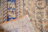 Distressed Oushak rug with folded corner exposing foundation, showing blue, orange, ivory patterns.