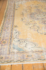 Distressed Oushak rug: pale dusty gold field with etched texture, scrolling vines, faded lavender border.