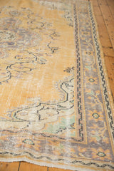 Distressed vintage Oushak rug corner showing etched golden pile and faded floral border.