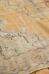 Distressed texture of vintage Oushak rug, showing faded gold, ivory, and pale green tones.
