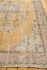 Distressed Oushak rug showing worn dusty gold field, etching to foundation, and pale floral border.
