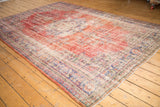 Distressed corner of vintage Oushak rug with faded cherry red, dusty navy, and ivory patterns.