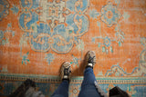 Distressed vintage Oushak rug, tangerine orange field, sky blue floral vinery, faint foundation.
