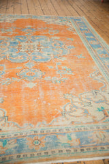 Distressed Oushak carpet texture with faded tangerine orange and sky blue floral motifs.