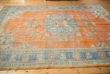 Distressed tangerine orange vintage Oushak rug corner, showing sky blue floral border.