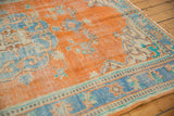 Distressed vintage Oushak rug close-up: tangerine orange field, sky blue floral border, visible pattern wear.